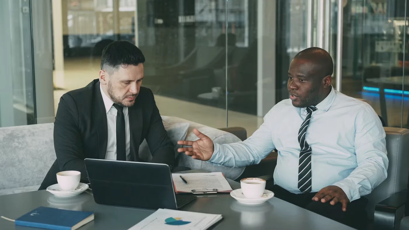 Two professionals talking through a project over coffee with a laptop and documents