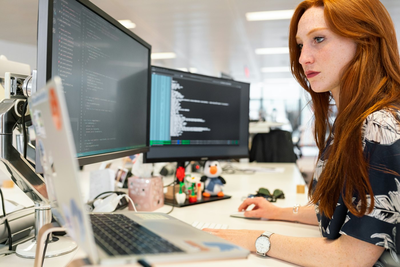 A woman working at a desk with multiple monitors in an open office